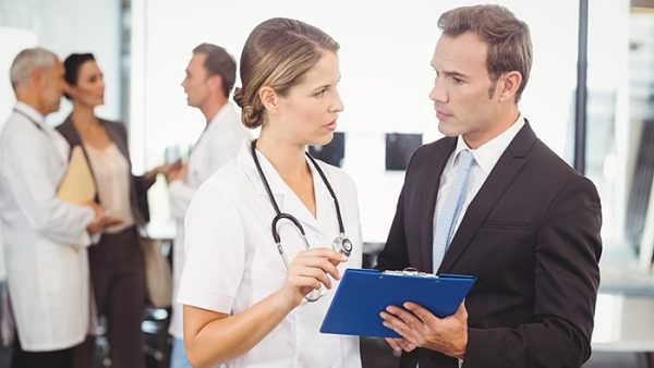 Female practitioner chats with businessman holding clipboard