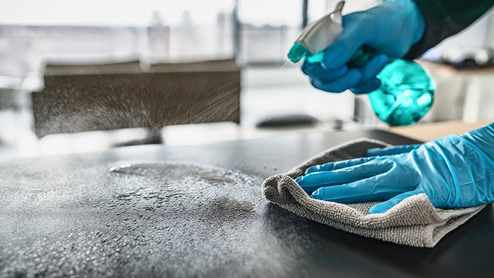 Sanitizing surfaces cleaning home kitchen table with disinfectant spray bottle washing surface with towel and gloves. COVID-19 prevention sanitizing inside.